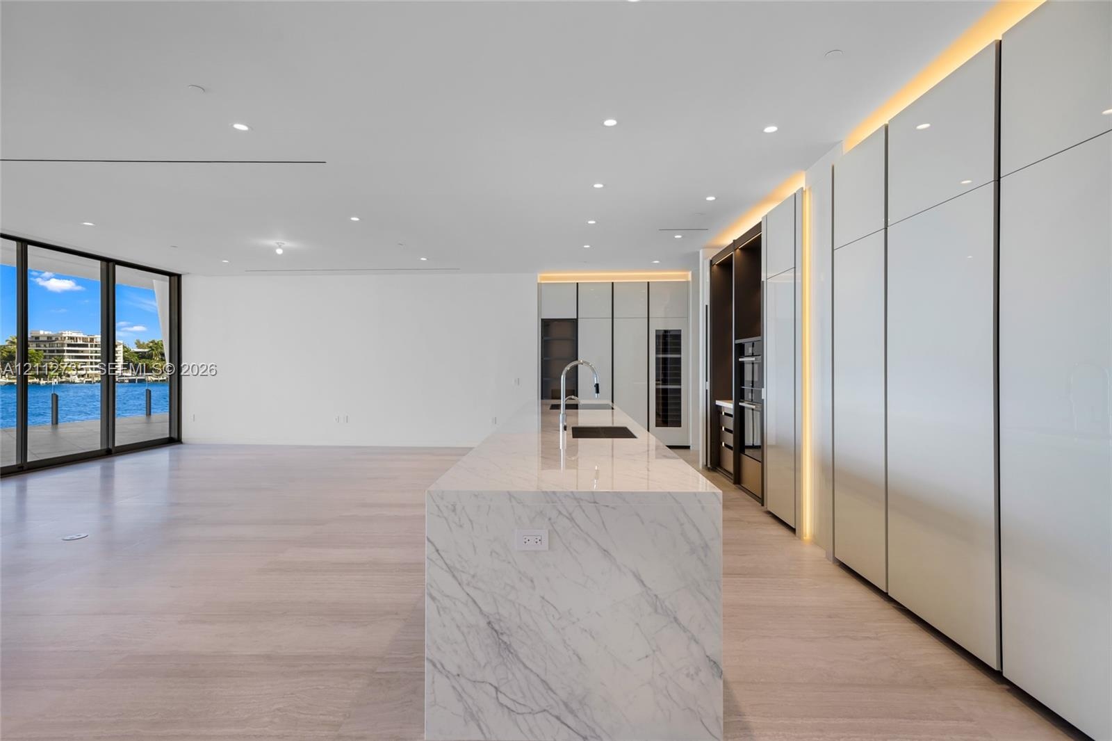 Kitchen featuring a stone-surface island, floor-to-ceiling high-gloss cabinetry, integrated lighting, wood-finish flooring, and expansive glass slidin