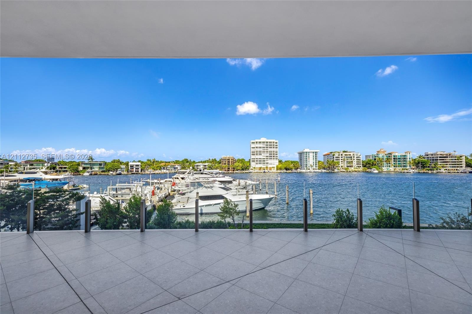 Covered terrace featuring large-format porcelain tile flooring and a transparent glass railing overlooking the waterfront