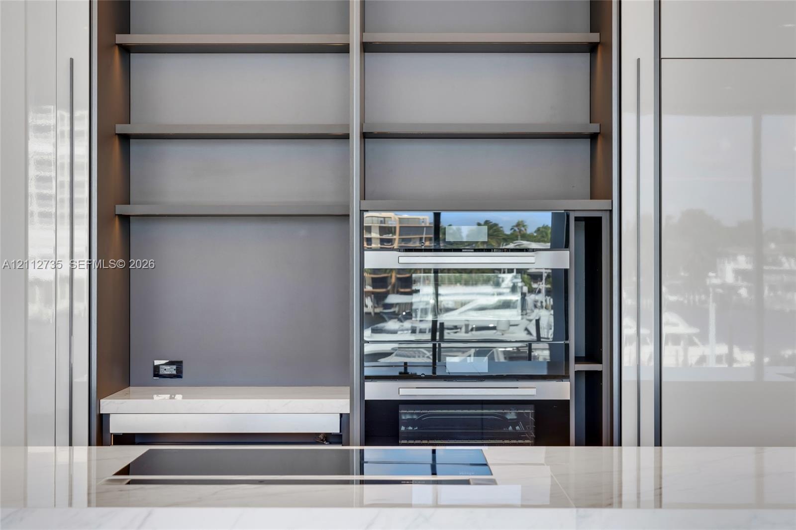 Floor-to-ceiling cabinetry with open shelving, integrated stainless steel double wall ovens, smooth-surface cooktop, and stone countertop