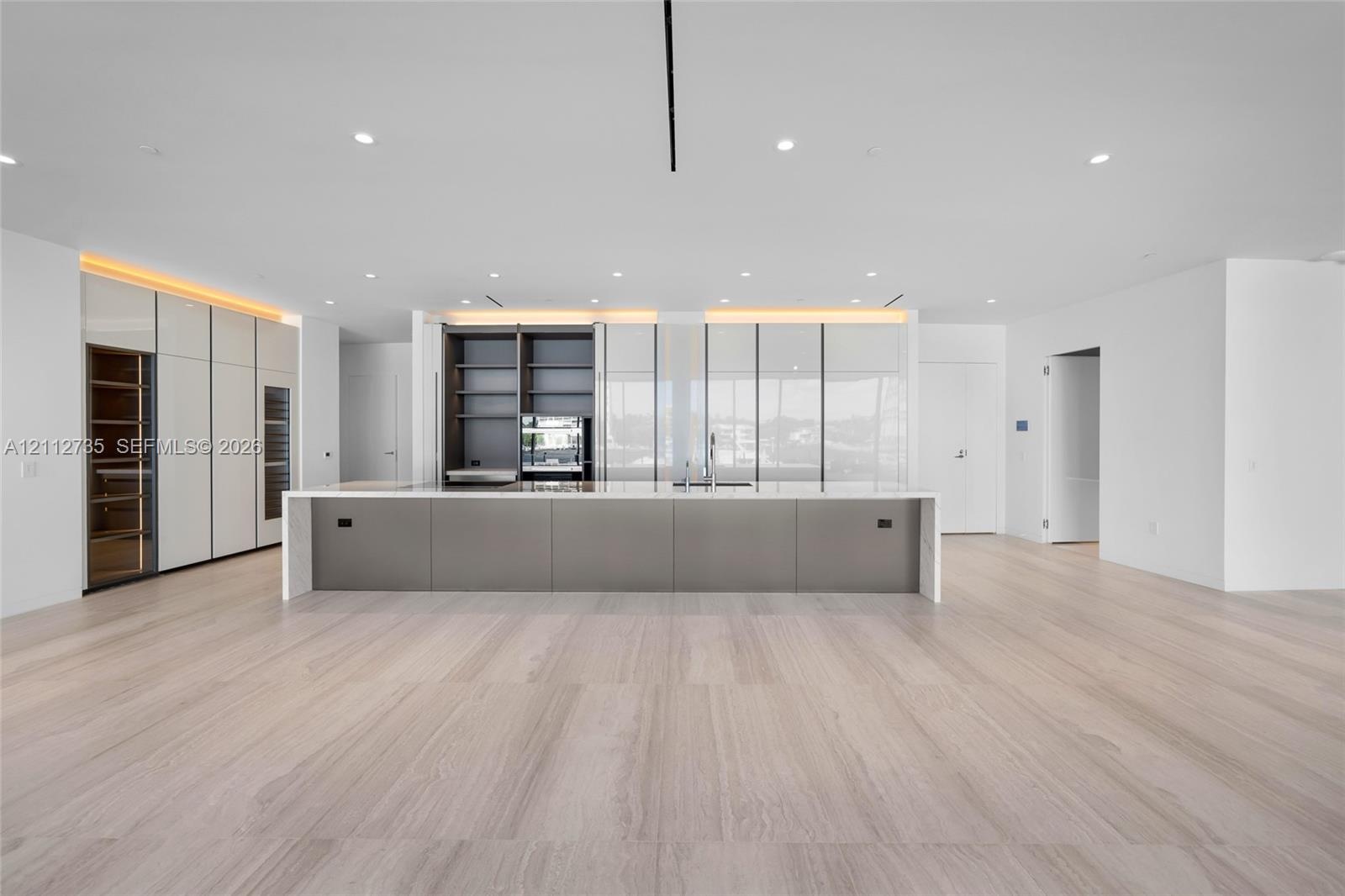 Minimalist kitchen featuring an expansive center island with a stone countertop, floor-to-ceiling cabinetry with integrated display shelving, built-in