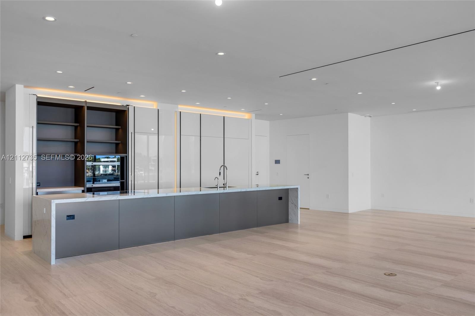 Modern kitchen featuring a expansive island with stone waterfall countertops, high-gloss white cabinetry, integrated open shelving, matte-finish lower