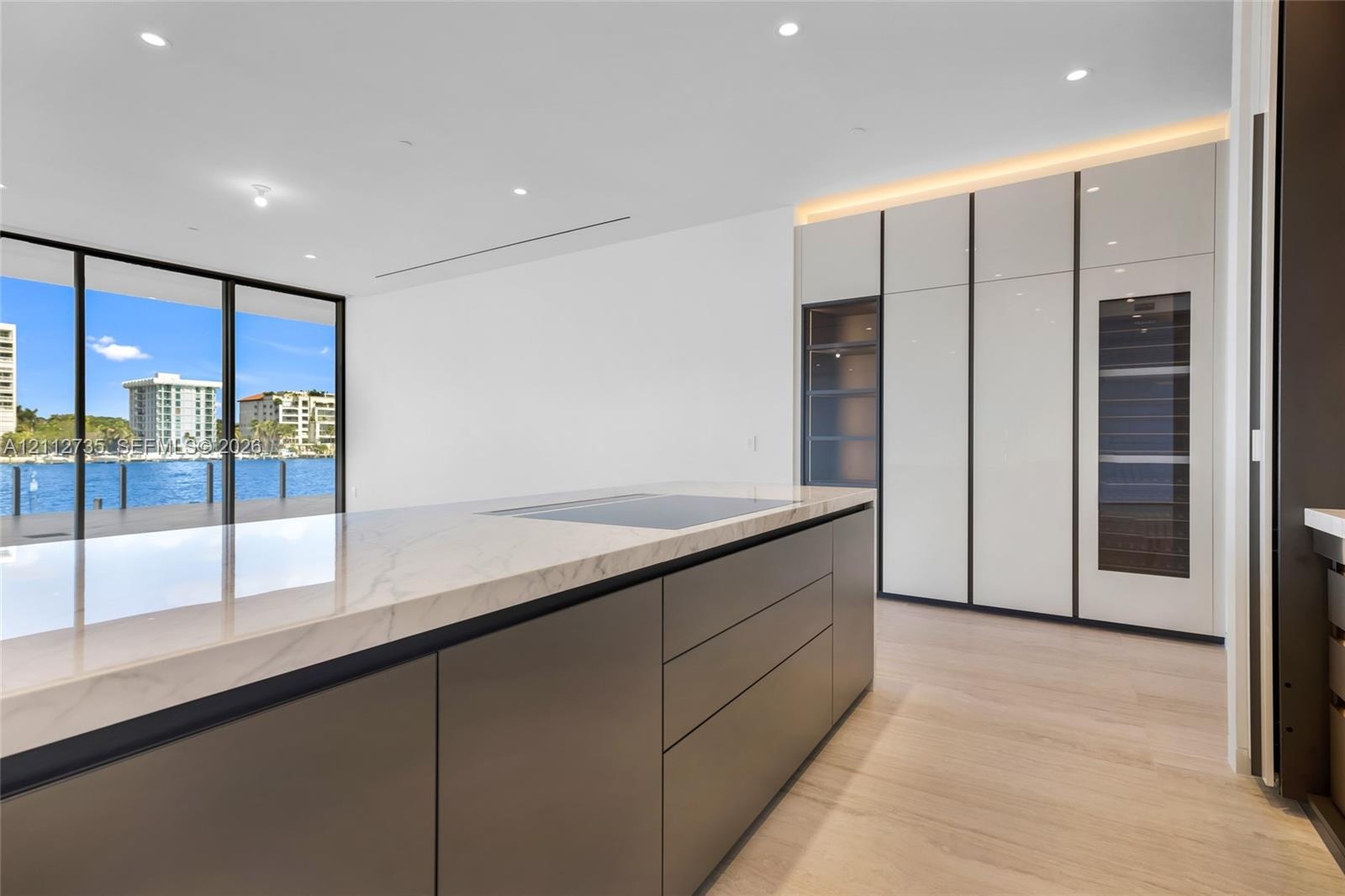 Kitchen featuring a large central island with a stone countertop and integrated cooktop, full-height gloss cabinetry with built-in refrigeration, wood