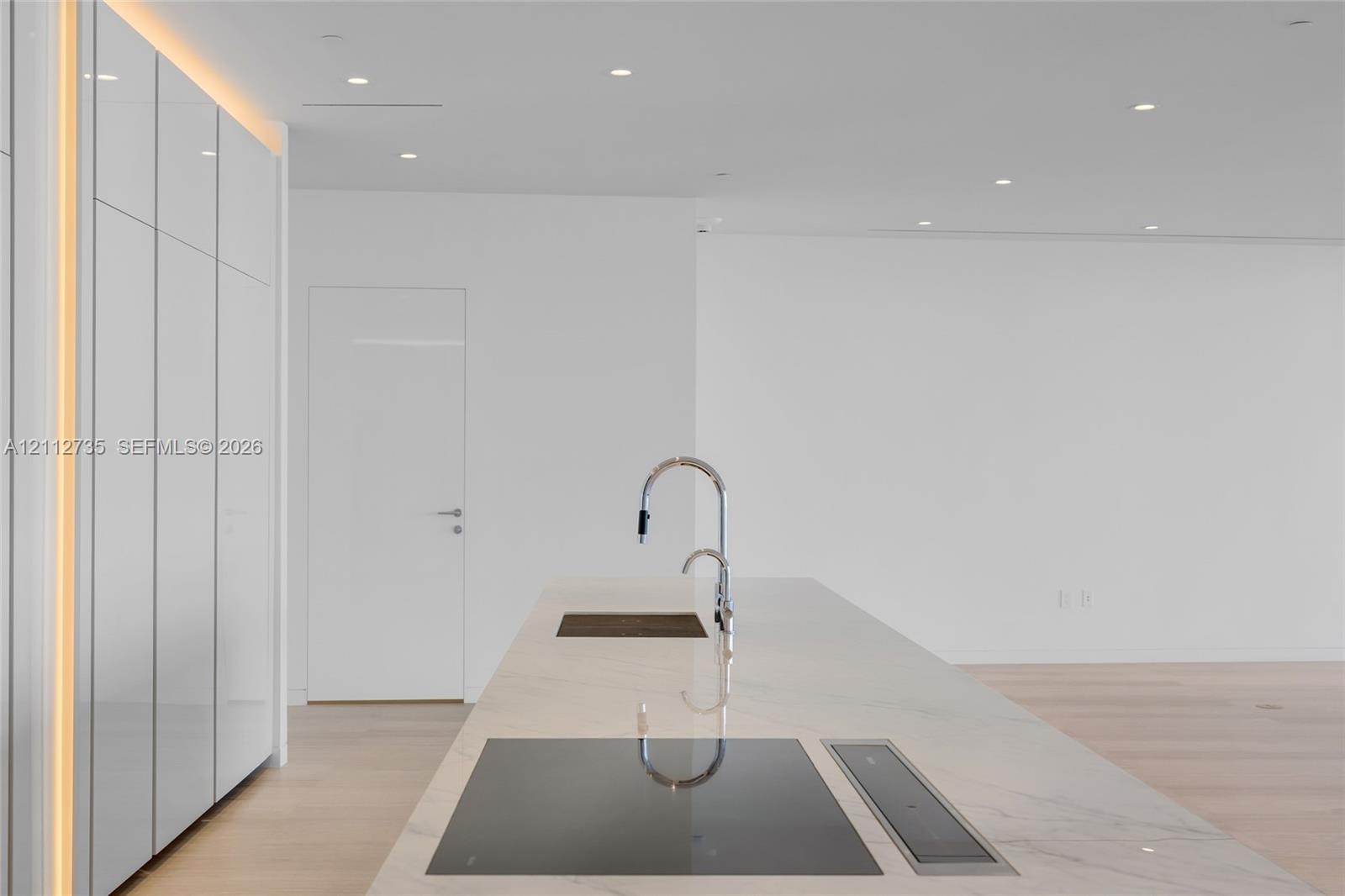 Minimalist kitchen island featuring a stone countertop, flush-mount cooktop, integrated downdraft ventilation, and a high-arc faucet, complemented by 