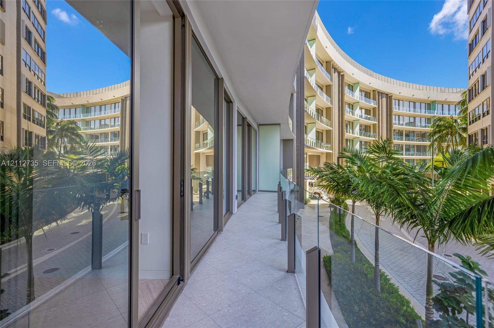 Covered balcony featuring expansive glass sliding doors, stone-tiled flooring, and a frameless glass balustrade