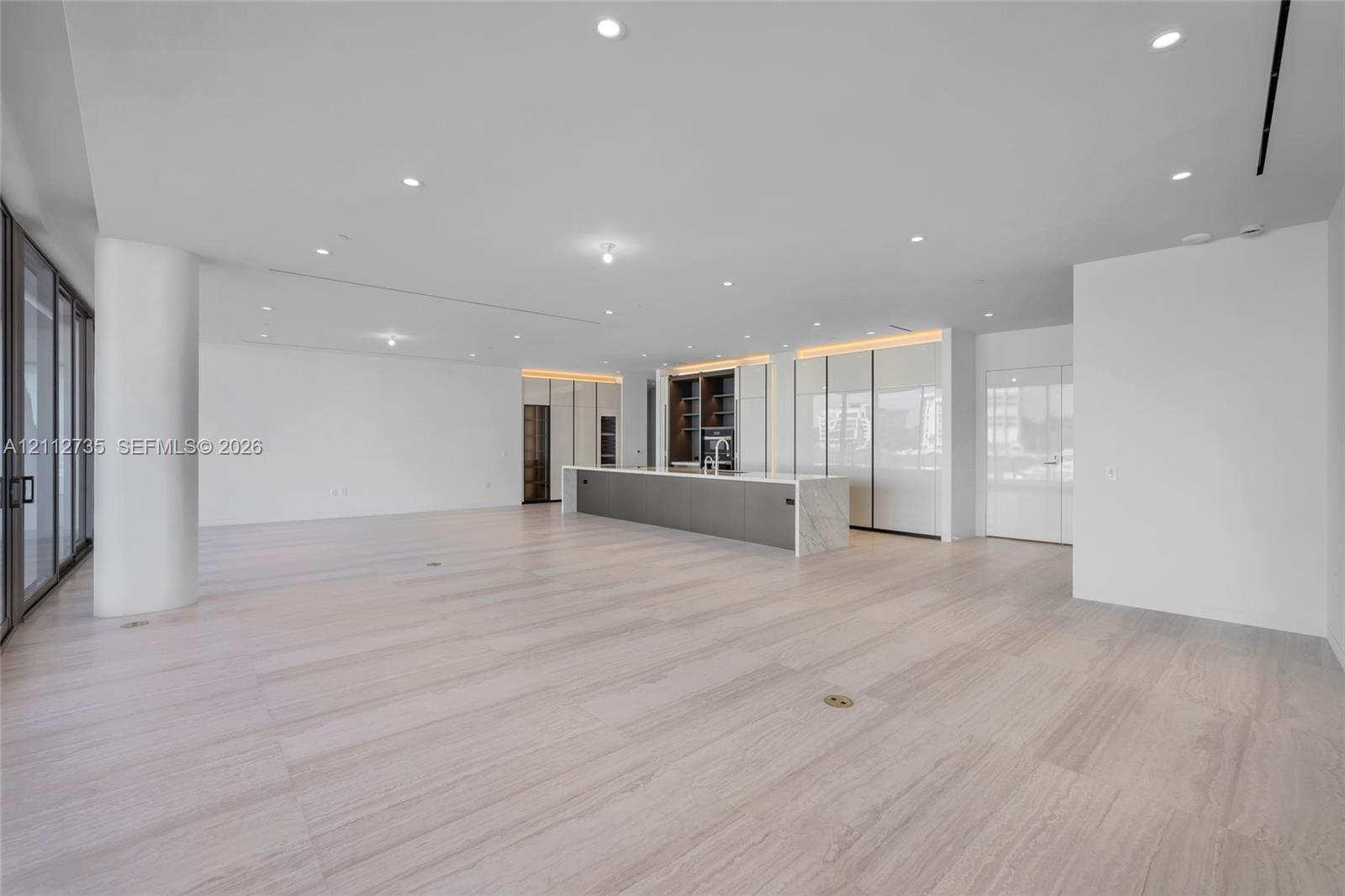 Open-concept space featuring light-toned wood-finish flooring, recessed ceiling lighting, floor-to-ceiling glass sliding doors, and a kitchen island w