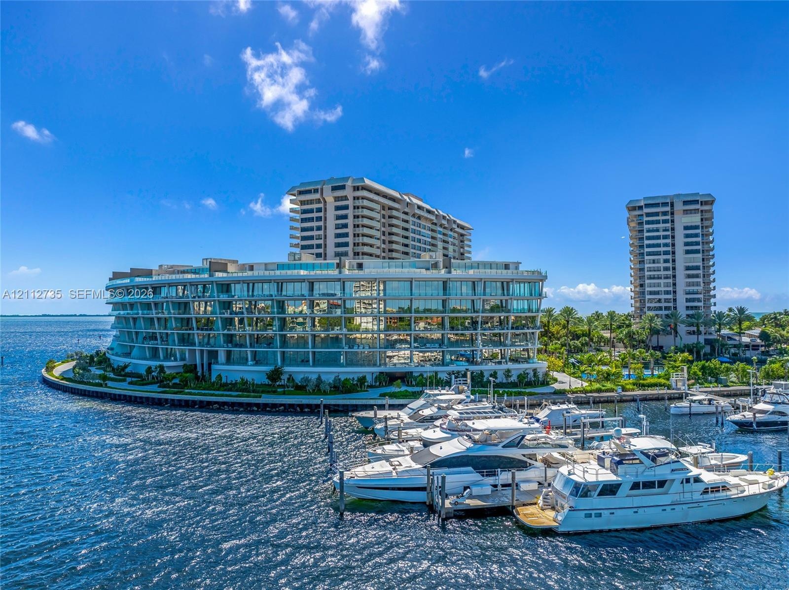Waterfront residential complex featuring floor-to-ceiling glass paneling, wraparound structural balconies, and a dedicated deep-water boat slip marina