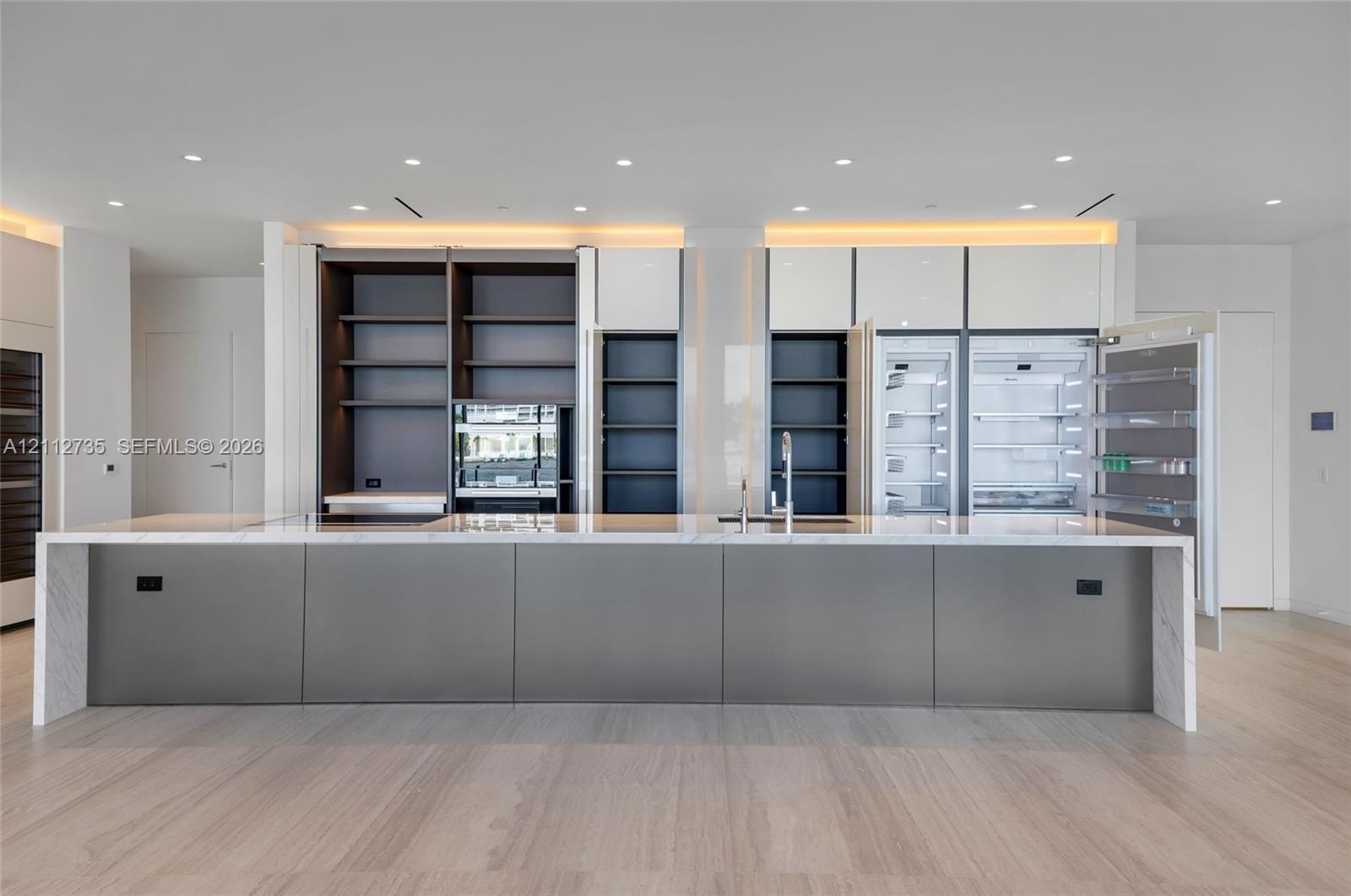 Large kitchen island featuring a stone waterfall countertop, integrated refrigeration, floor-to-ceiling cabinetry with open shelving, recessed lightin