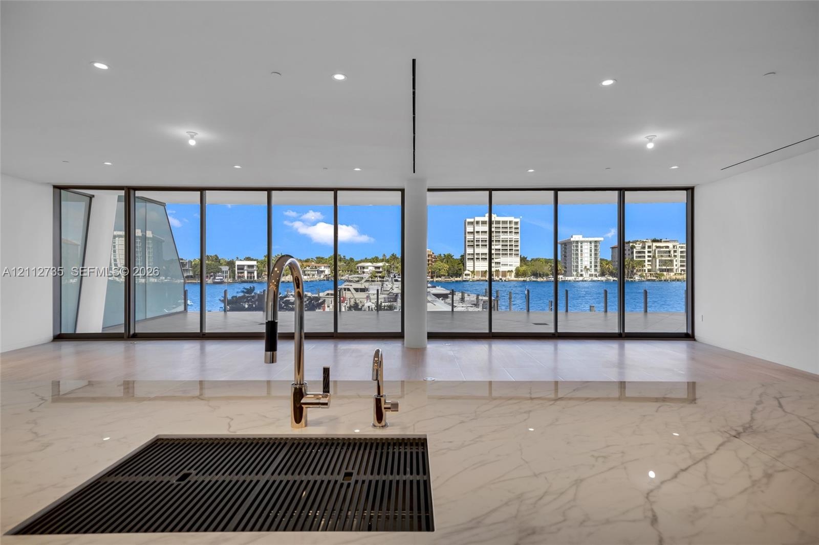 Countertop with an integrated drainboard and high-arc faucet, wood-finish flooring, and expansive floor-to-ceiling glass panels overlooking the waterf