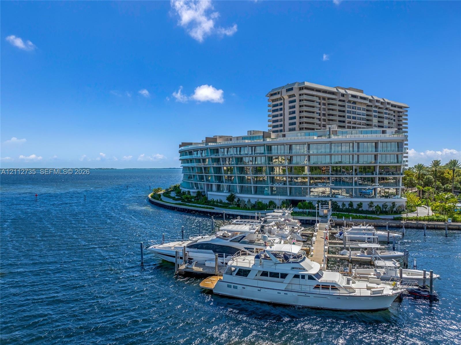 Waterfront multi-story residential building featuring floor-to-ceiling glass paneling, wraparound balconies, and a private deep-water marina