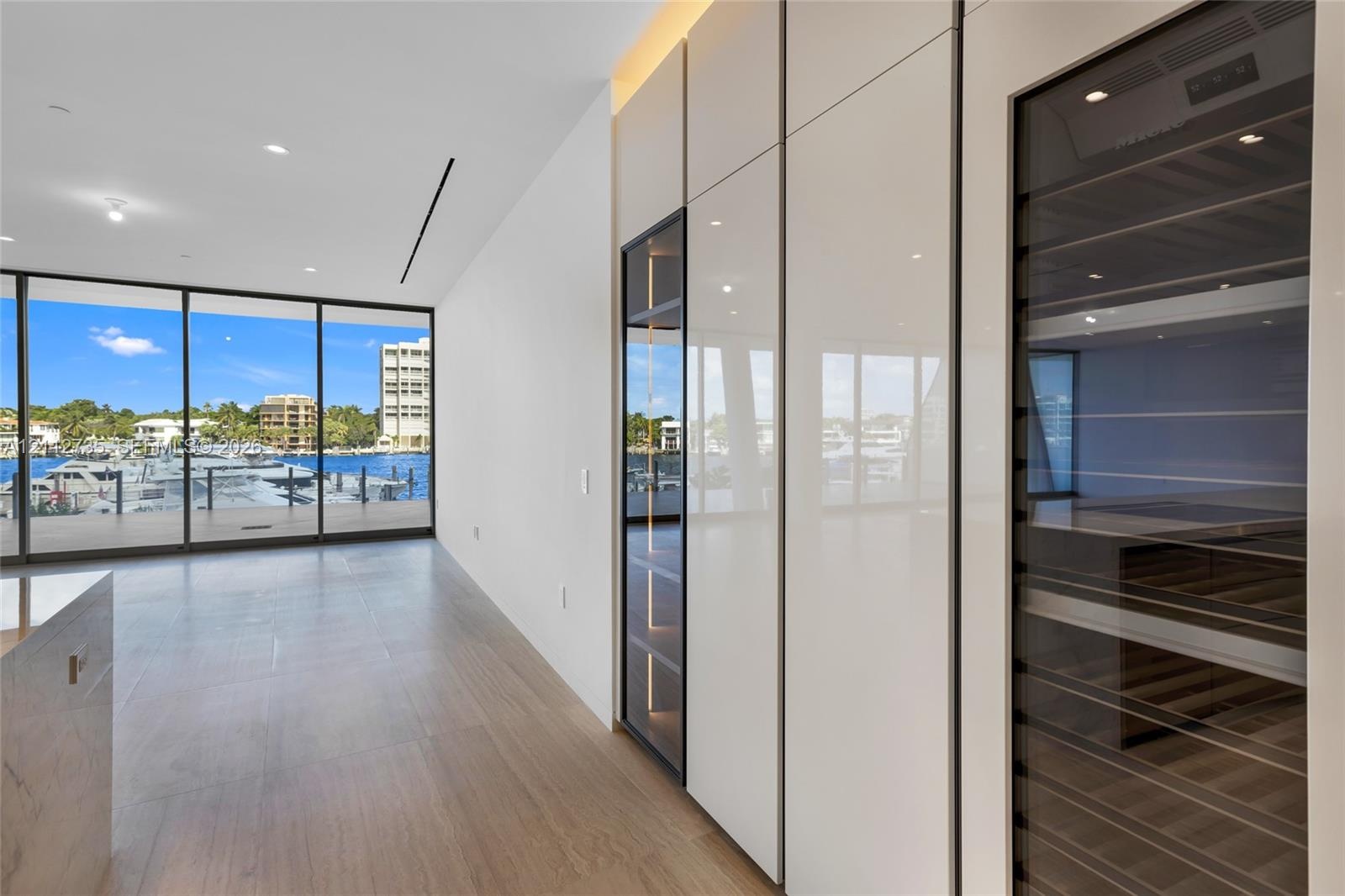 Floor-to-ceiling glass wall, custom cabinetry with high-gloss finish, integrated wine refrigeration, and wood-finish flooring