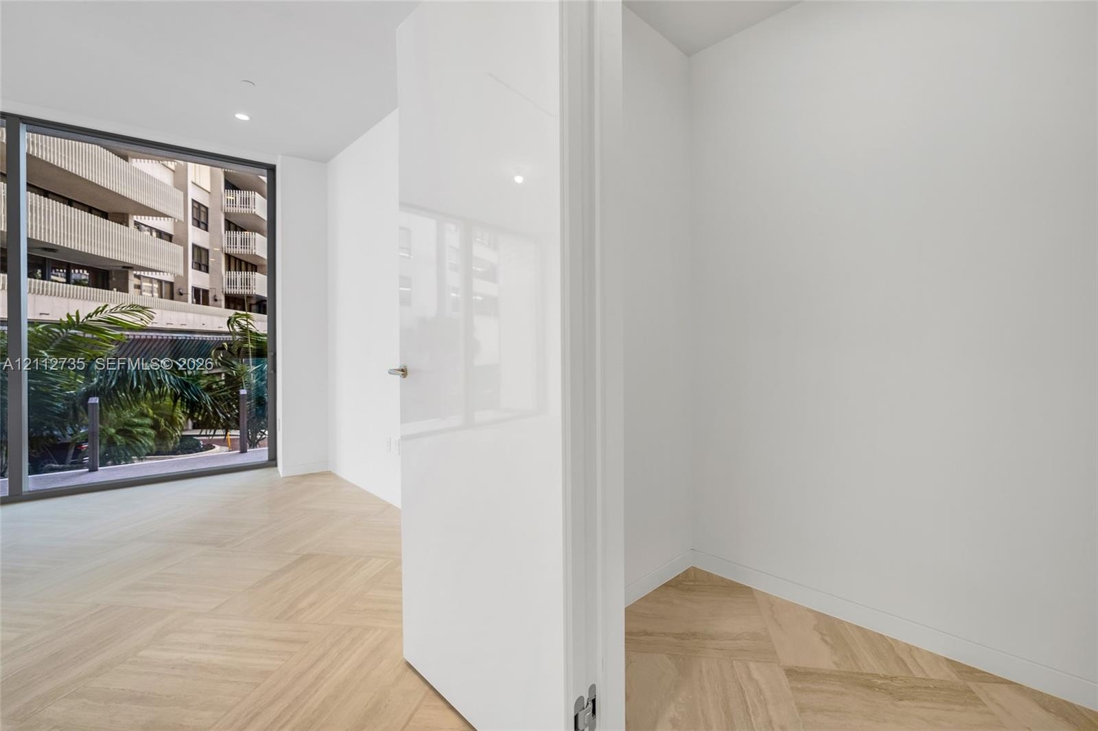 Herringbone-patterned wood-finish flooring, floor-to-ceiling glass window, and high-gloss white interior door