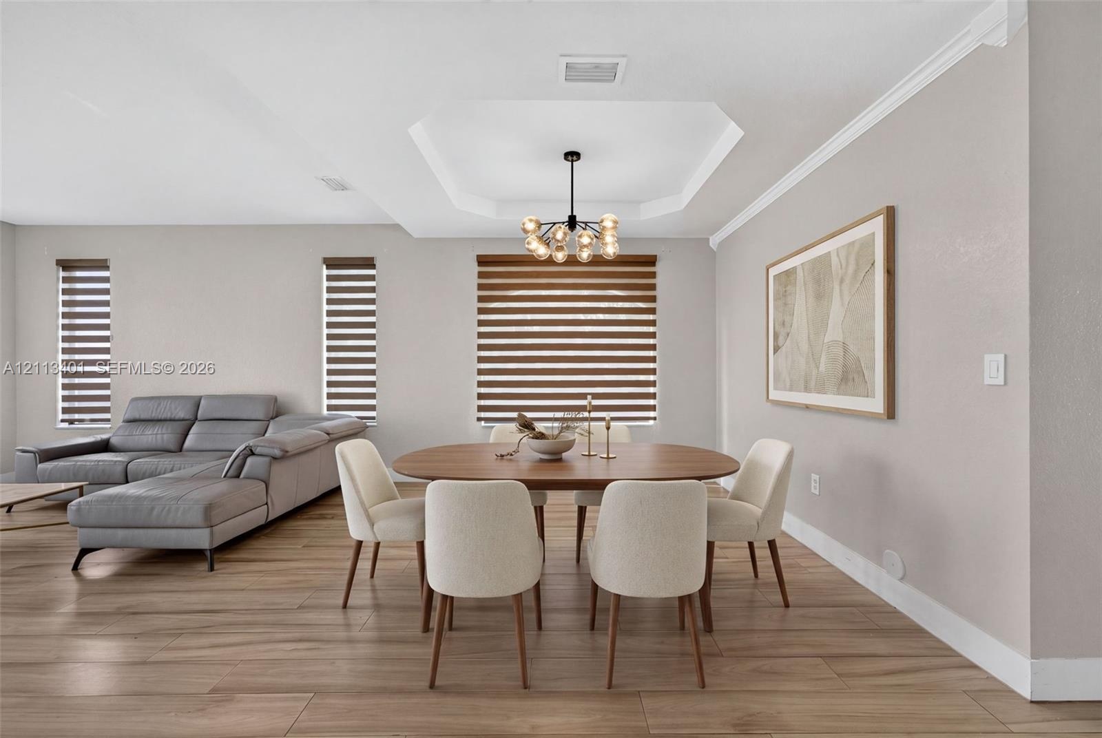 Tray ceiling, wood-finish flooring, multi-light orb chandelier, and dual-shade window treatments