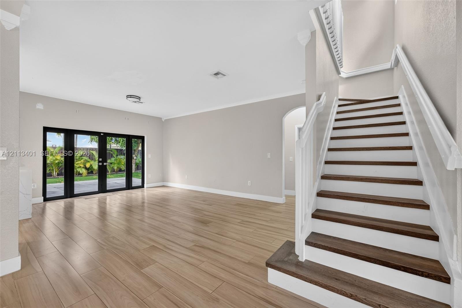 Open-concept interior featuring wood-finish flooring, a staircase with white balusters and dark wood-finish treads, crown molding, and black-framed gl