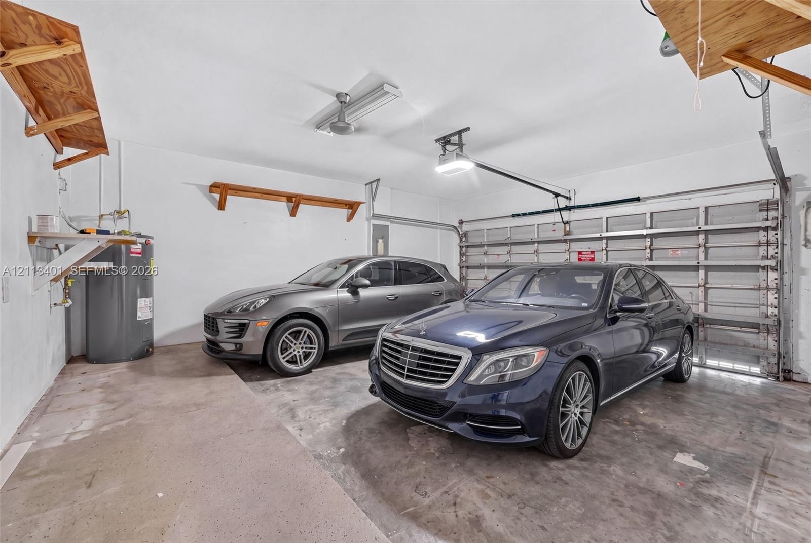 Two-car garage featuring a concrete floor, sectional overhead door, built-in wooden wall shelving, and a dedicated water heater