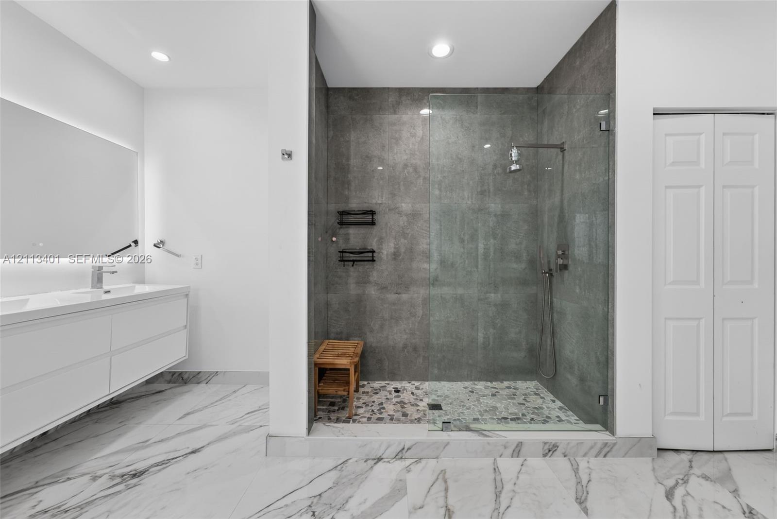 Floating dual-sink vanity with under-cabinet lighting, walk-in shower with frameless glass enclosure, floor-to-ceiling stone-look wall tile, pebble-te