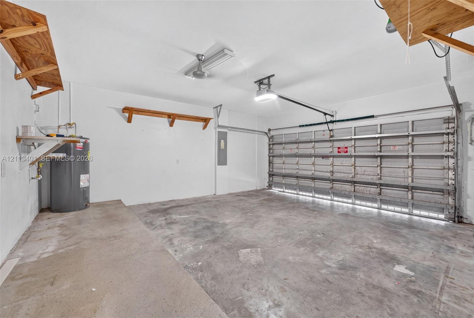 Two-car garage featuring a concrete floor, built-in wooden wall shelving, overhead fluorescent lighting, an automated door opener, and a dedicated wat