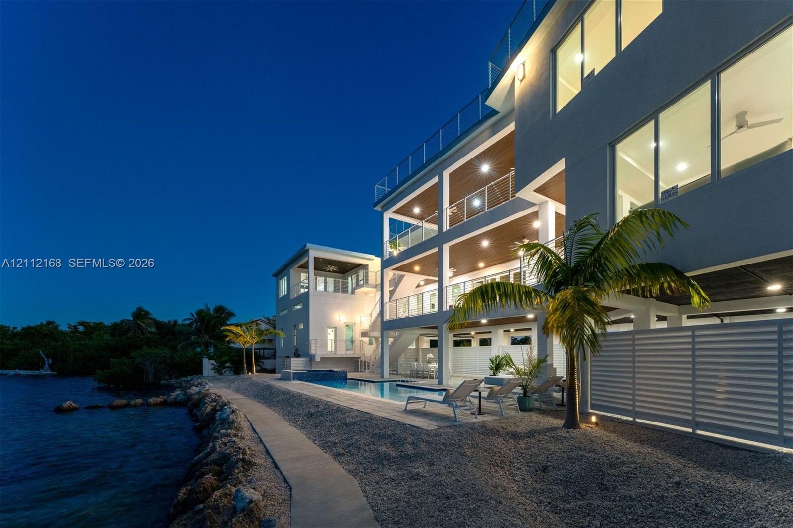 Multi-level exterior featuring stacked balconies with glass railings, a swimming pool with tile surround, and direct waterfront access via a rock-line