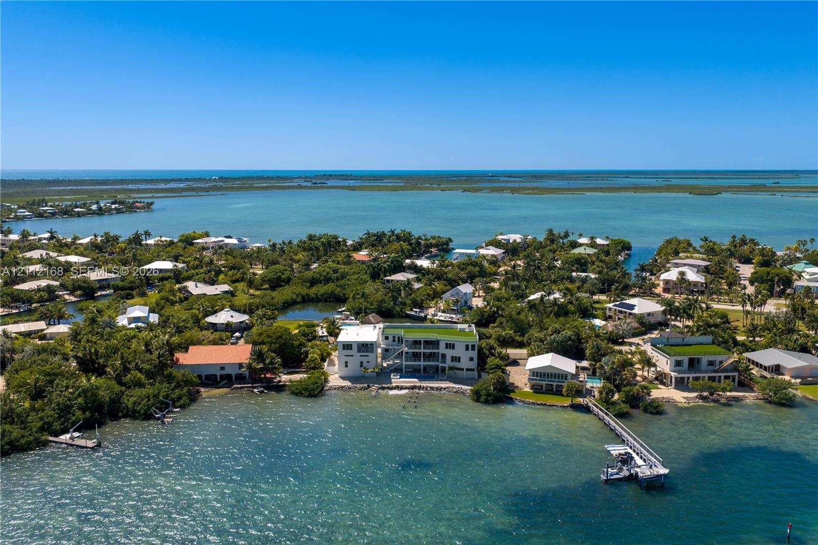 Waterfront estate featuring a multi-level structure with a flat roof, private dock, direct water access, and exterior balconies
