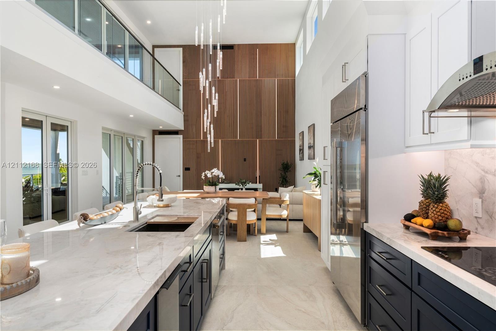 Double-height ceilings, floor-to-ceiling wood-panel accent wall, dual-tone cabinetry with stone-finish countertops, stainless steel integrated applian