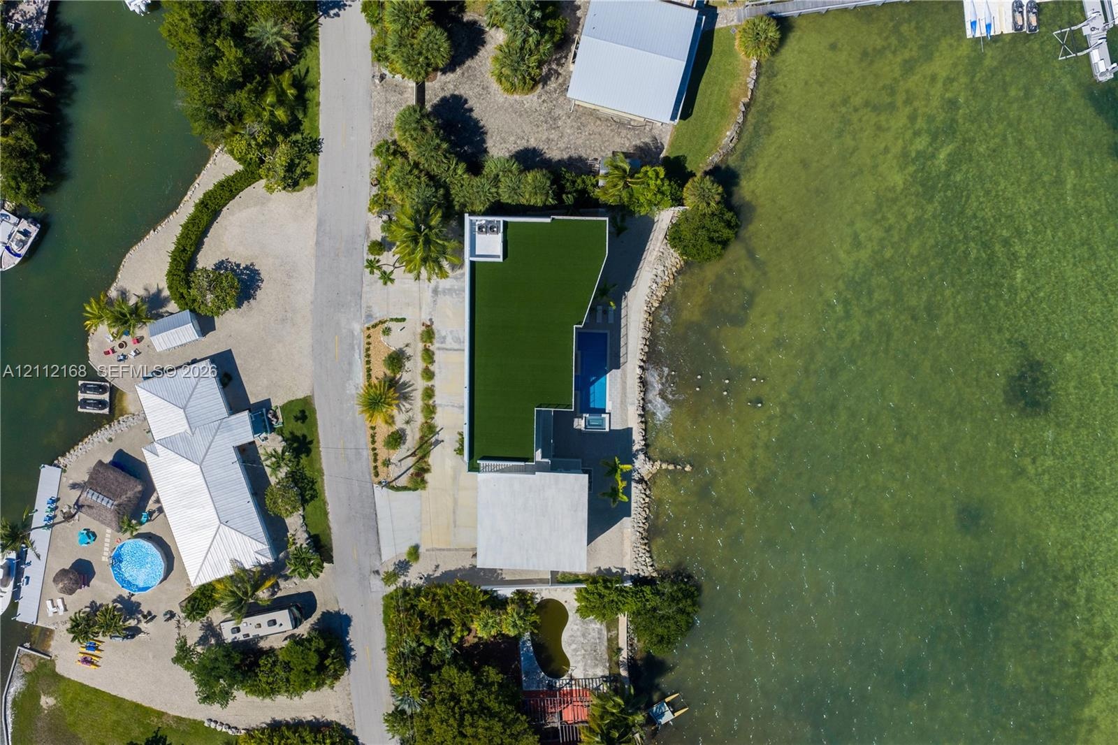 Waterfront estate featuring a direct shoreline, private swimming pool, concrete paved driveway, and artificial turf roof installation