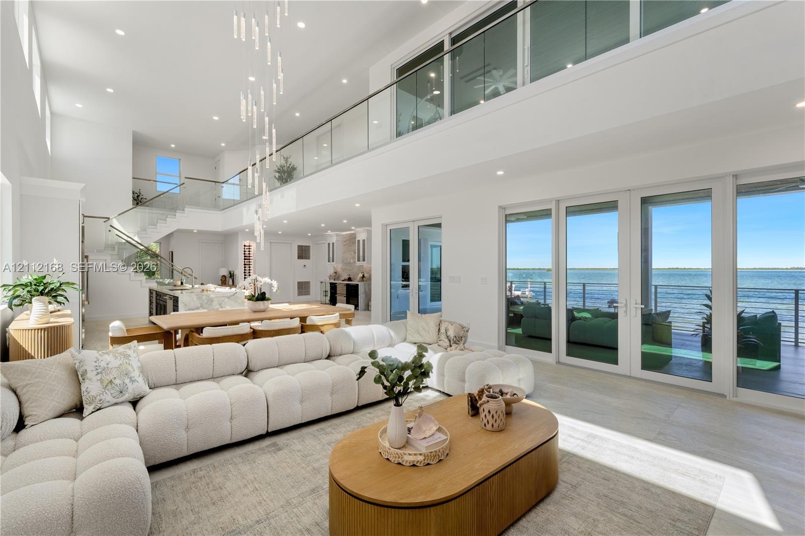 Expansive open-concept living area featuring double-height ceilings, a floor-to-ceiling glass-paneled mezzanine, multi-panel sliding glass doors, and 