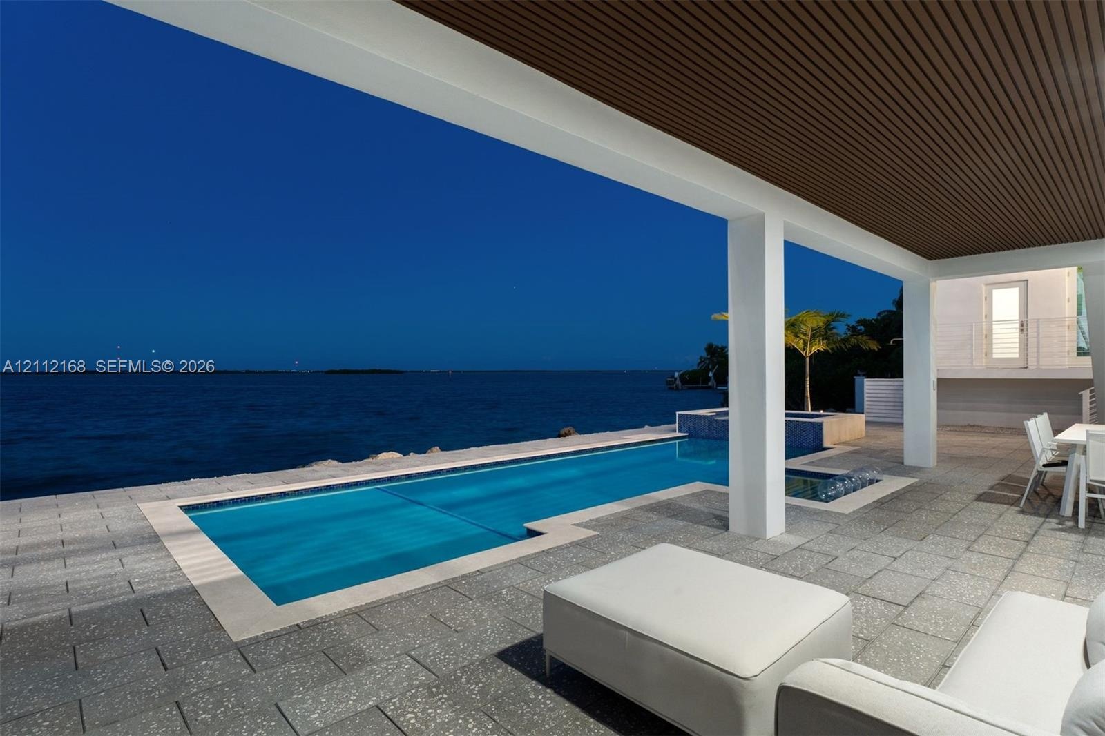 Covered patio with wood-slat ceiling, natural stone tile flooring, swimming pool, built-in spa, and water frontage
