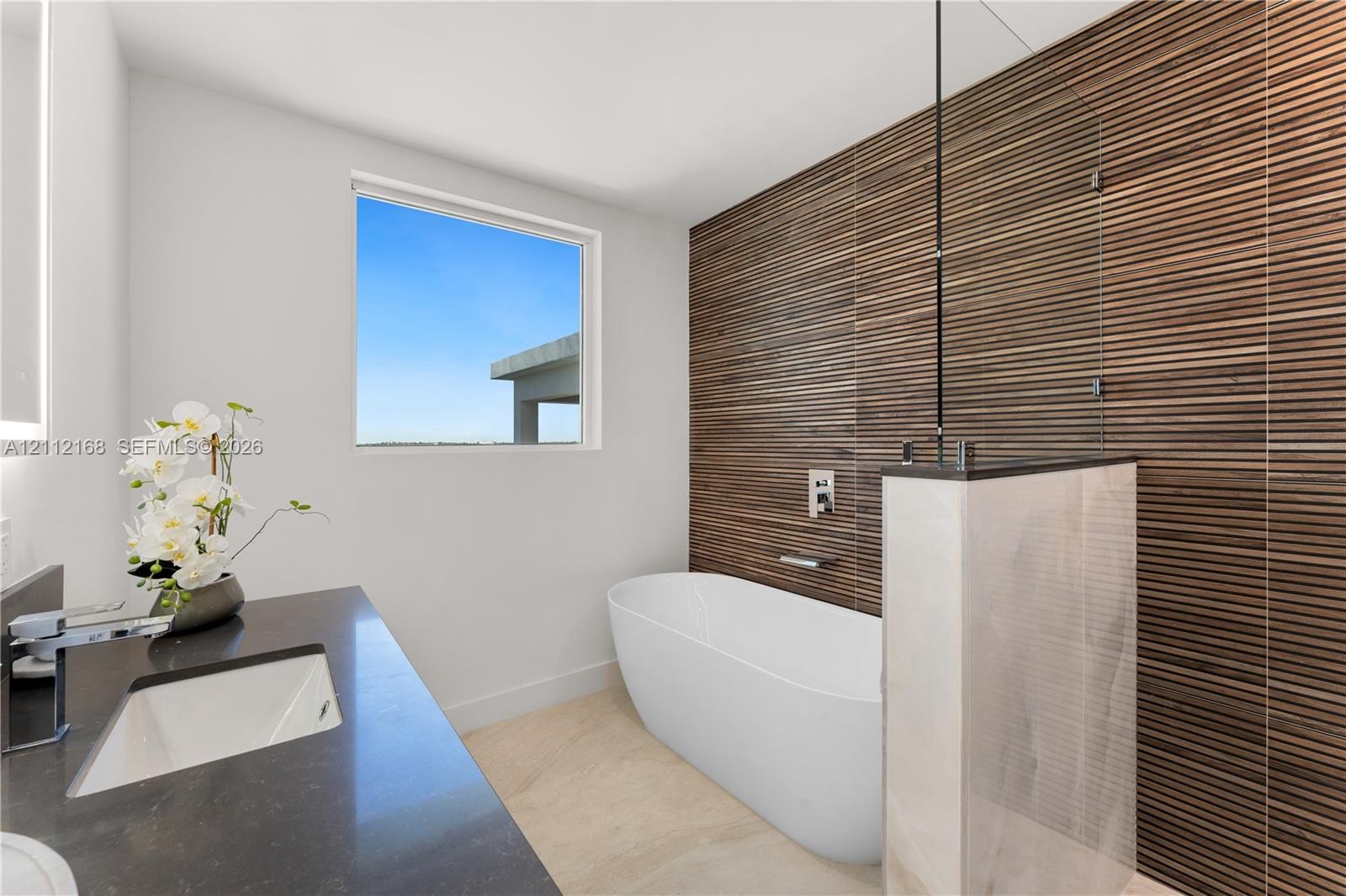 Freestanding soaking tub featuring a wall-mounted faucet, horizontal slatted wood-texture accent wall, glass partition, stone-finish vanity countertop