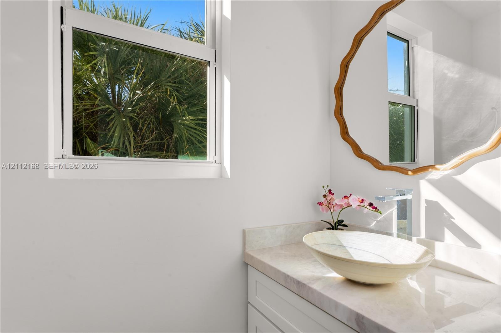 Vanity featuring a stone-surface countertop, an oval vessel sink, a chrome single-handle faucet, and white shaker-style cabinetry, complemented by a s