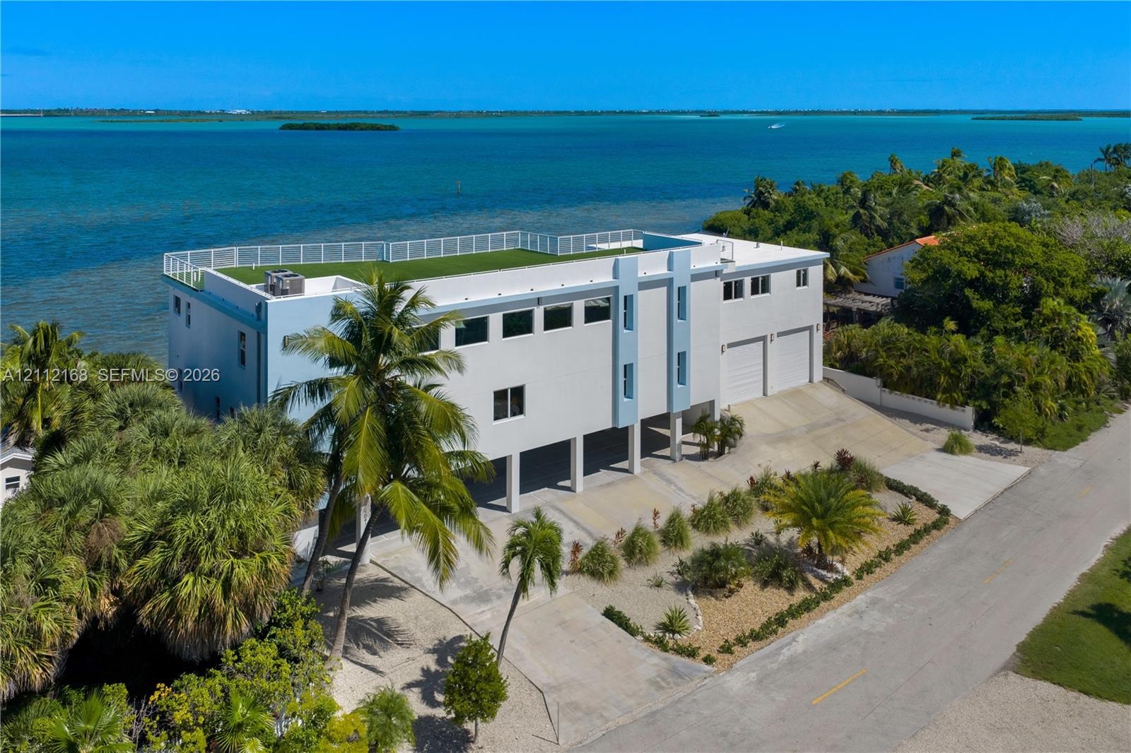 Waterfront residence featuring a rooftop terrace, elevated construction, concrete driveway, and attached two-car garage