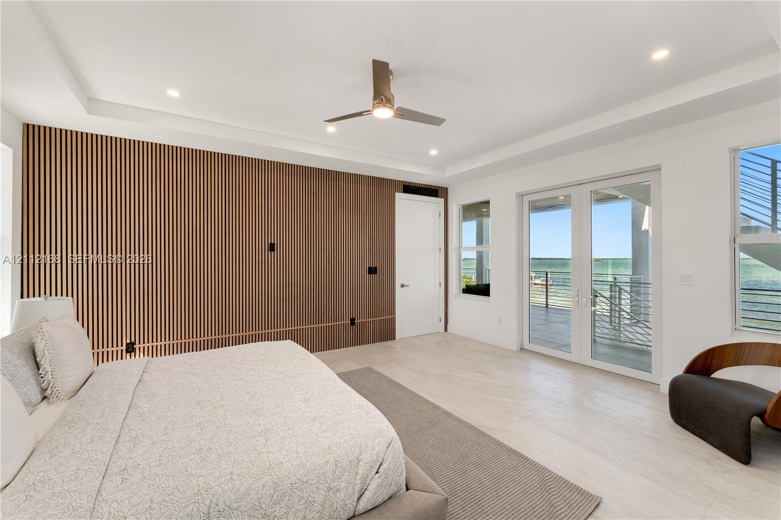 Slatted wood-finish accent wall, tray ceiling with recessed lighting, light-toned wood-finish flooring, and glass French doors leading to an exterior 