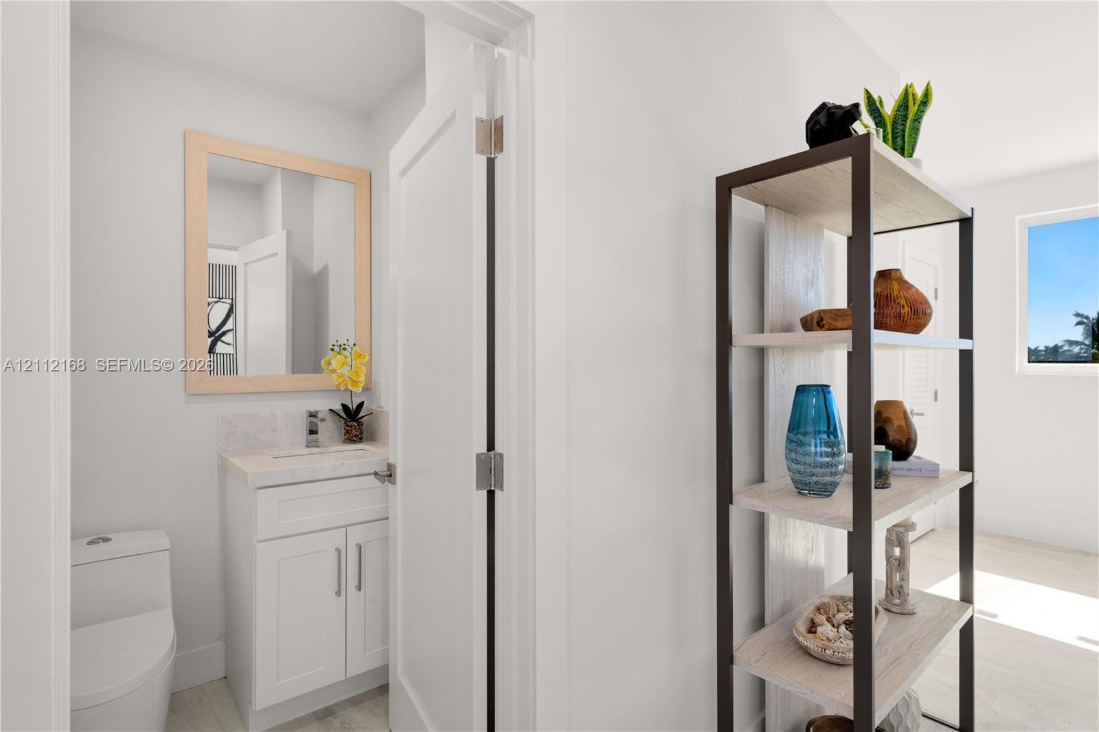White cabinetry with stone-surfaced countertop, integrated under-mount sink, polished chrome faucet, and rectangular mirror with light wood-finish fra