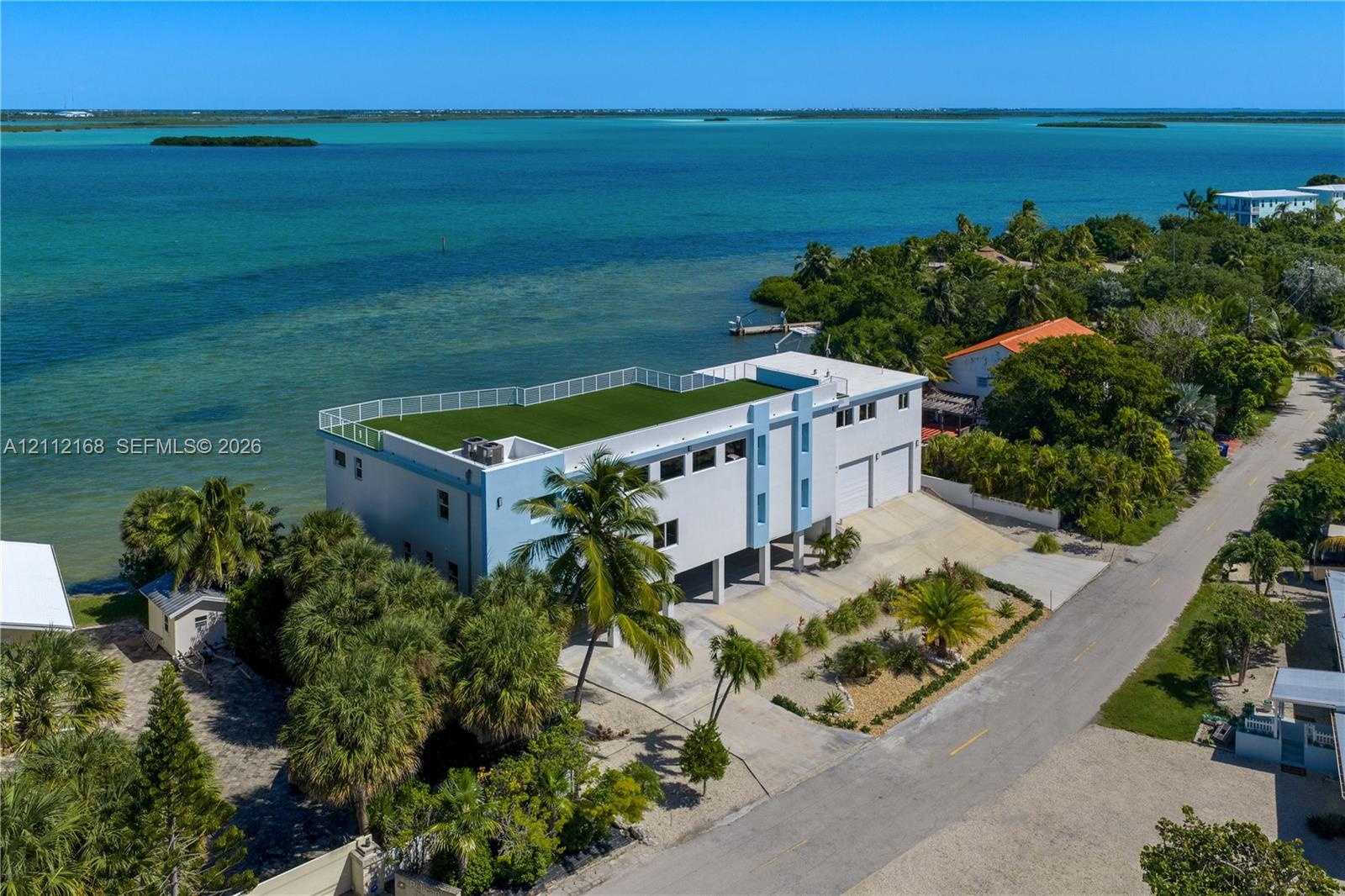 Waterfront multi-story residence featuring a rooftop terrace with synthetic turf, perimeter railing, paved driveway, and attached two-car garage