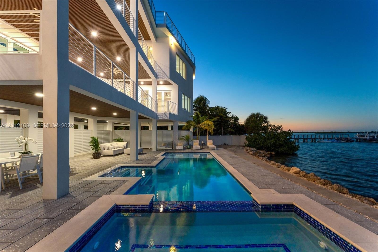 Waterfront multi-level residence featuring a custom swimming pool with integrated spa, expansive covered lanais, metal cable railings, and textured st