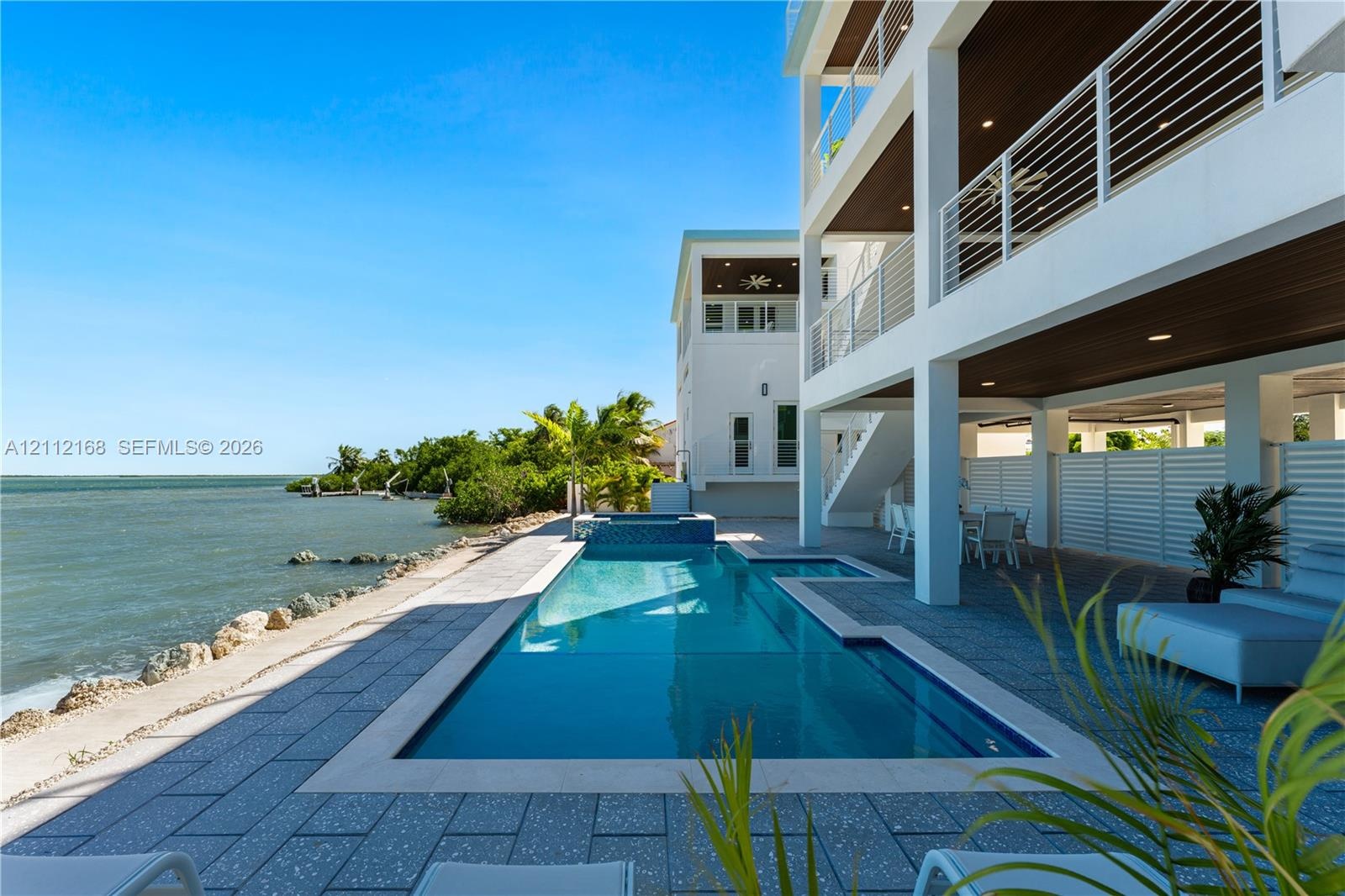 Waterfront exterior featuring a multi-level structure with recessed balconies, horizontal cable railings, a rectangular swimming pool with an integrat