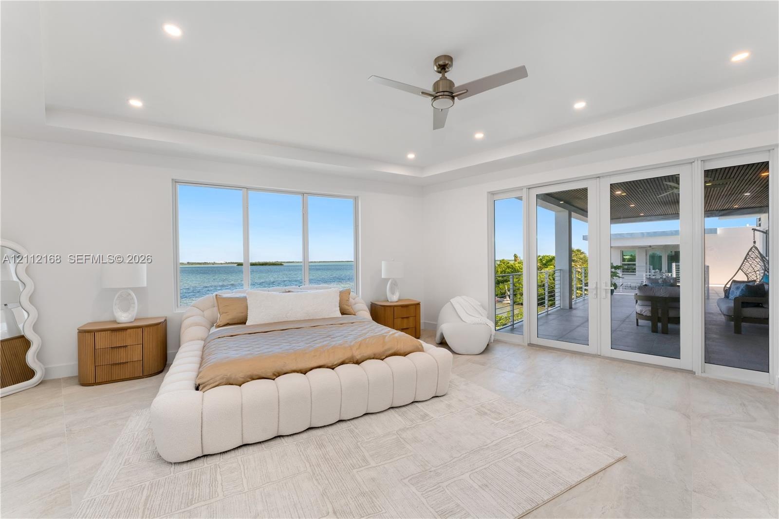 Tray ceiling with recessed lighting, ceiling fan, large windows, and floor-to-ceiling glass panel doors opening to a covered terrace
