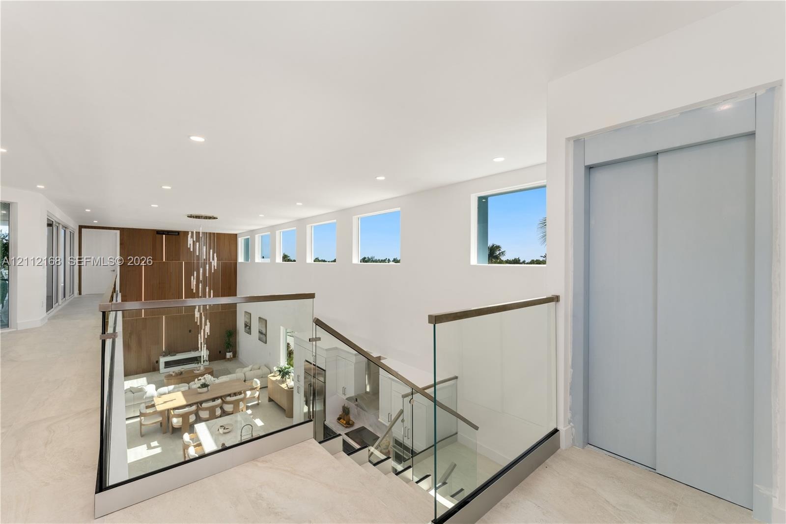 Open landing featuring large-format tile flooring, a glass-panel railing with a wood-finish handrail, a private elevator, recessed ceiling lighting, a