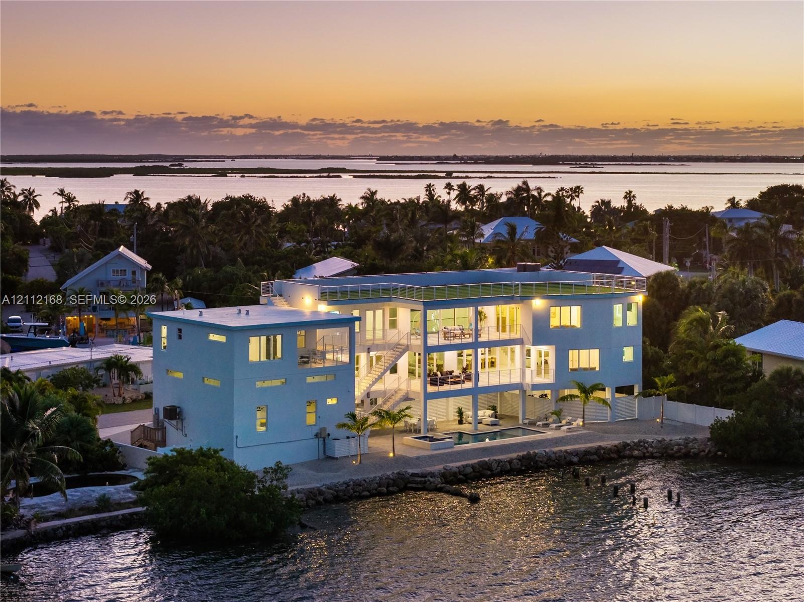 Multi-level waterfront residence featuring a rooftop deck, exterior staircase, ground-level pool, and stone-reinforced shoreline