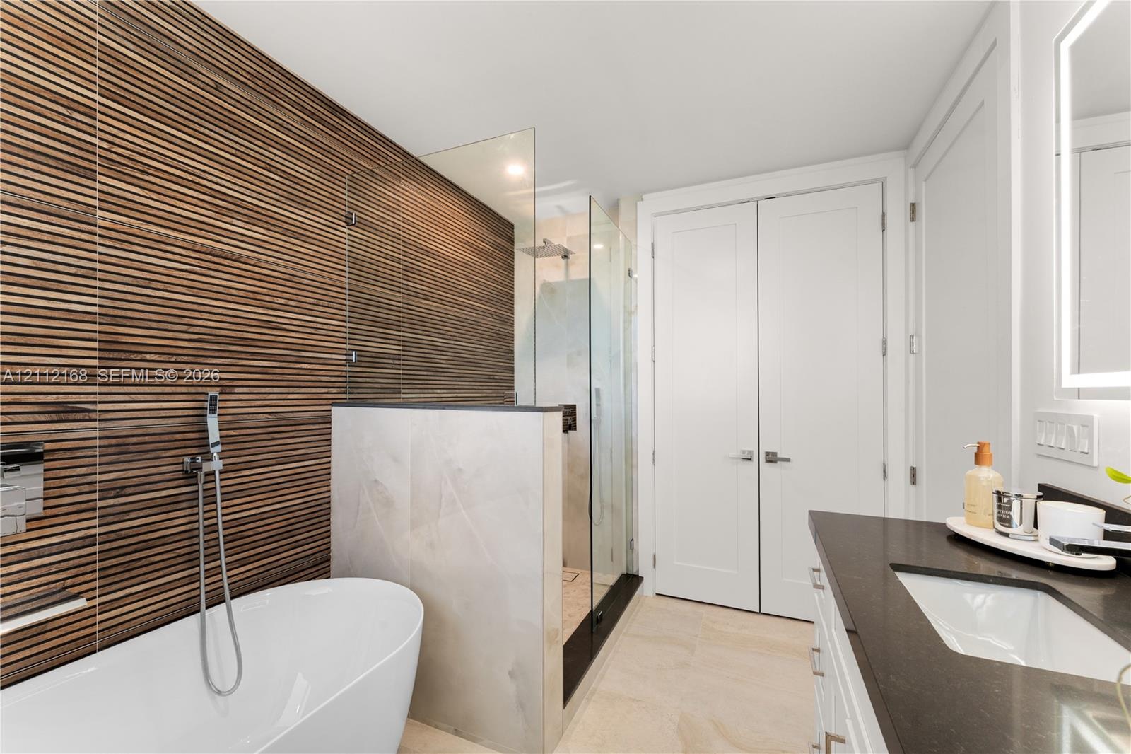 Bathroom featuring a textured wood-slat feature wall, freestanding soaking tub, walk-in glass-enclosed shower, dark countertop with an integrated basi