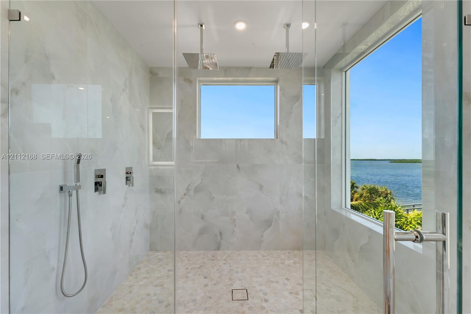 Walk-in shower featuring floor-to-ceiling stone-patterned tile, dual ceiling-mounted rainfall showerheads, a handheld sprayer, a glass enclosure, and 