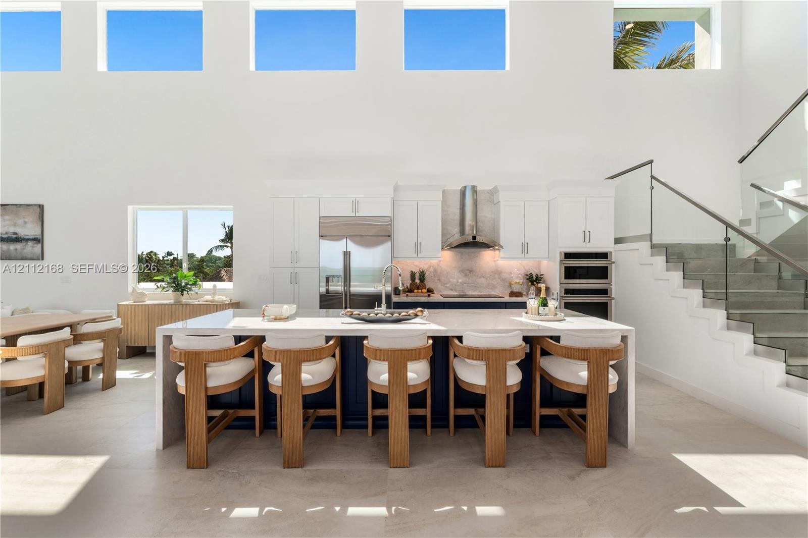 Double-height ceilings with transom windows, large center island with waterfall countertop, stainless steel kitchen appliances, and glass-paneled stai