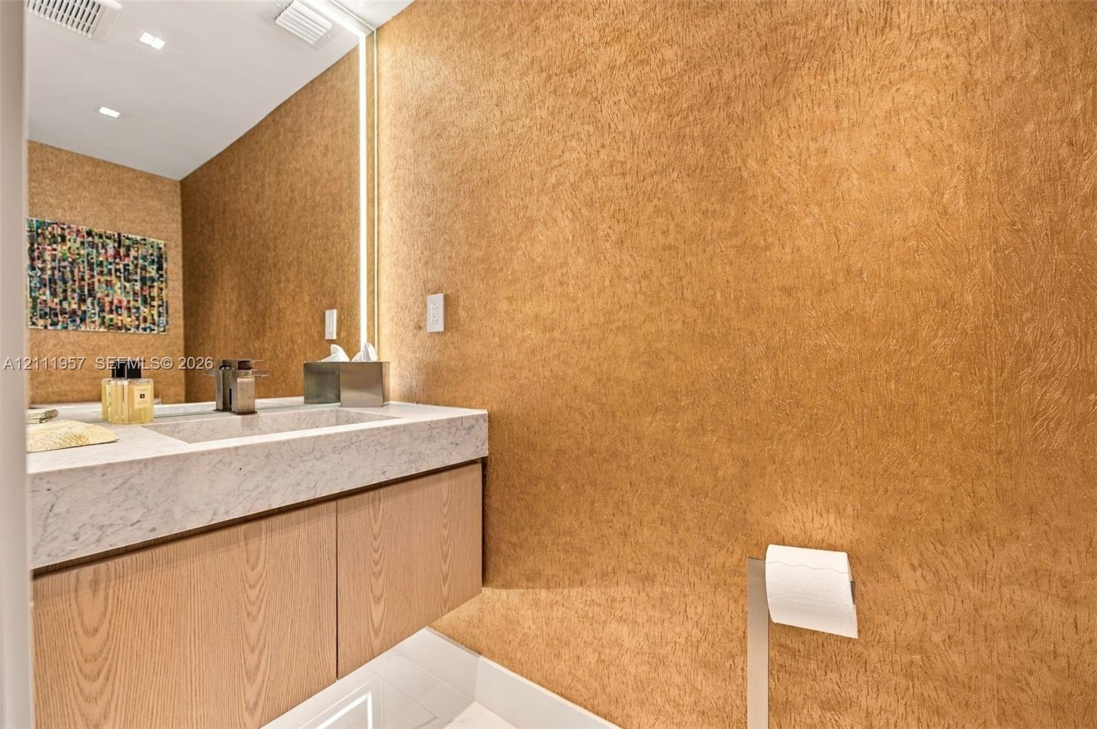 Textured wall finish, floating vanity with wood-grain cabinetry, stone countertop, integrated vertical lighting, and recessed ceiling lighting