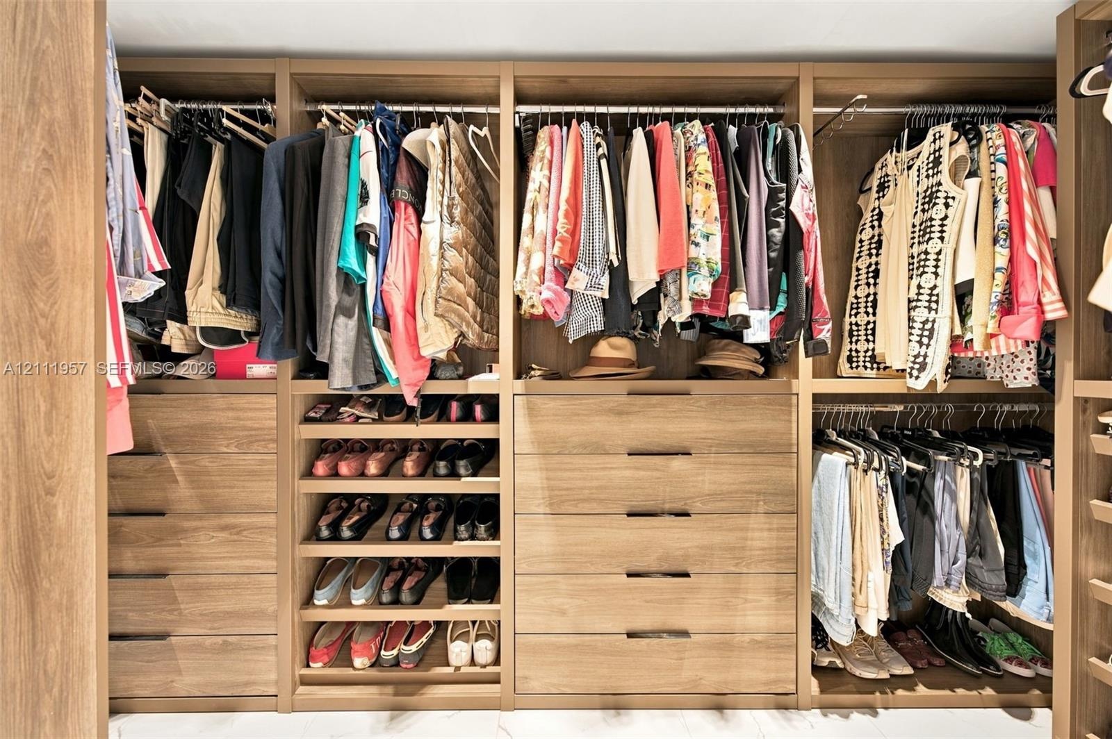 Custom closet organization system featuring wood-finish cabinetry, multi-tiered hanging rods, integrated shelving for footwear, and deep drawers with 