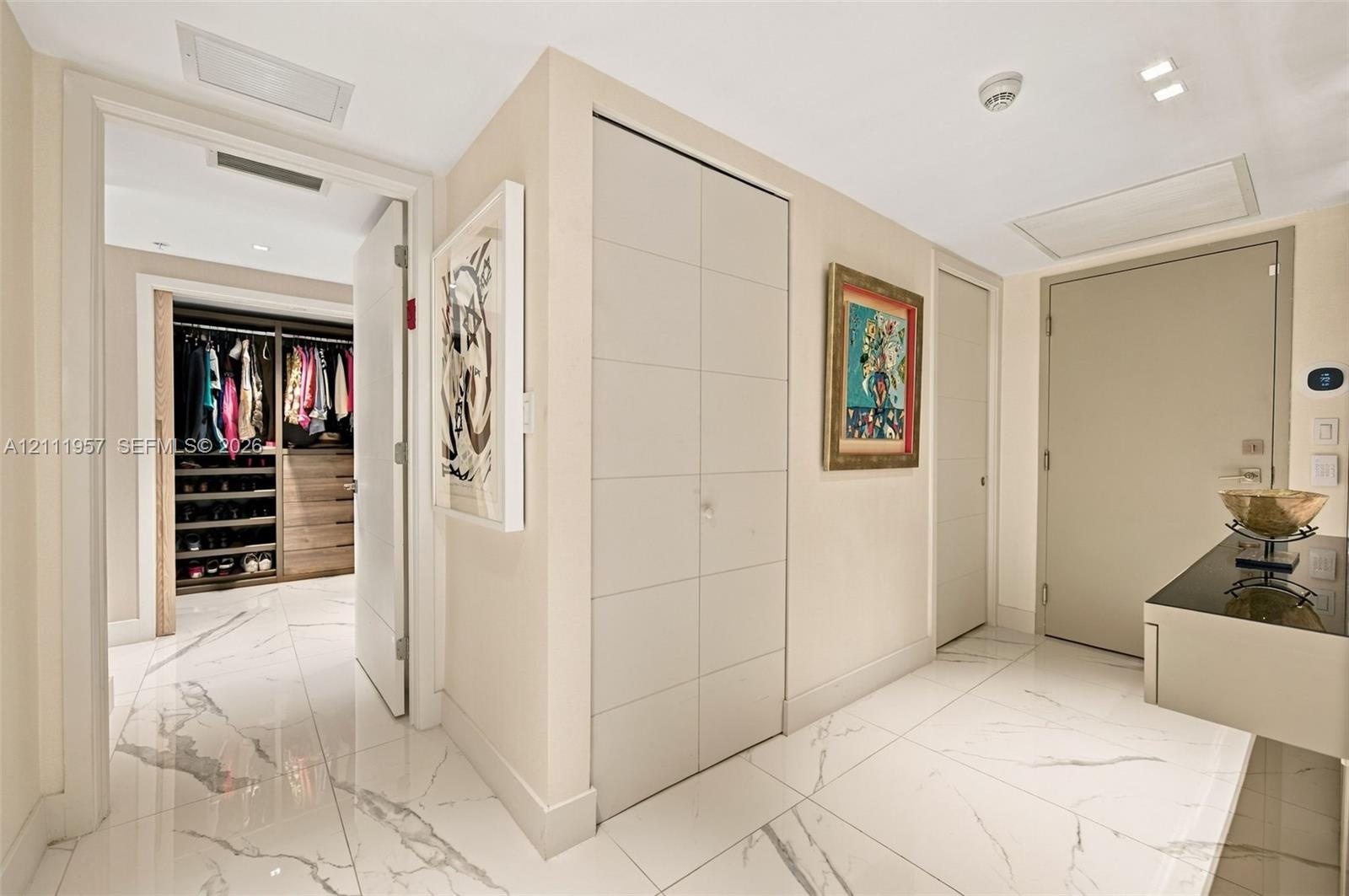 Large-format tile flooring, built-in floor-to-ceiling cabinetry with panel detailing, and custom walk-in closet featuring wood-finish shelving and dra
