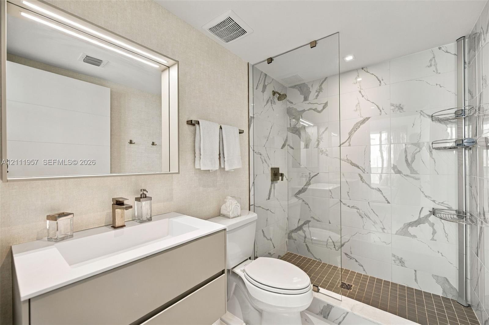 Floating vanity featuring a rectangular integrated sink, quartz countertop, and gold-tone faucet, complemented by a large framed vanity mirror, glass-