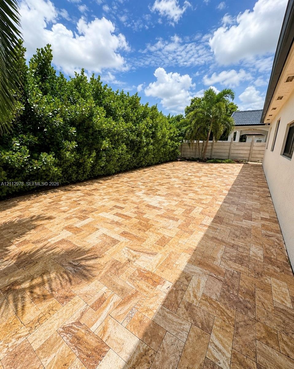 Outdoor patio area featuring herringbone-patterned stone pavers, privacy-focused mature hedge landscaping, and a perimeter concrete block wall