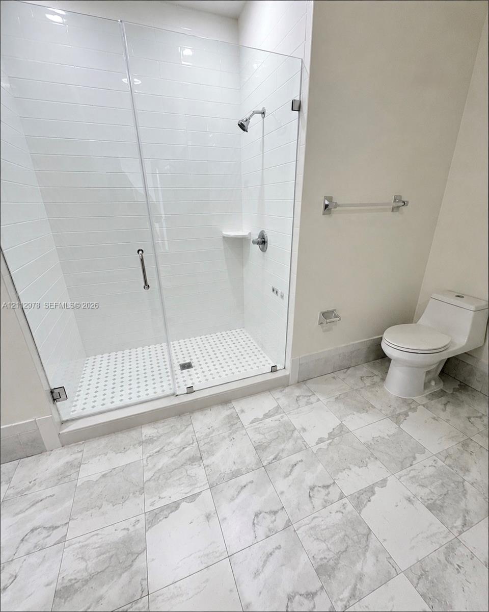 Walk-in shower featuring white subway tile surround, frameless glass door, and integrated shelving, complemented by stone-patterned floor tile and a d