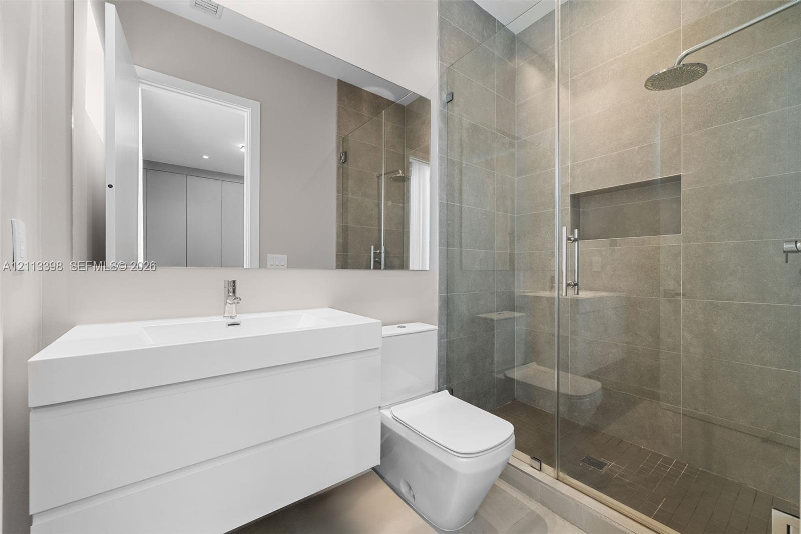 Modern wall-mounted vanity with integrated sink, full-width mirror, walk-in shower with floor-to-ceiling stone-finish tile, glass shower enclosure, an
