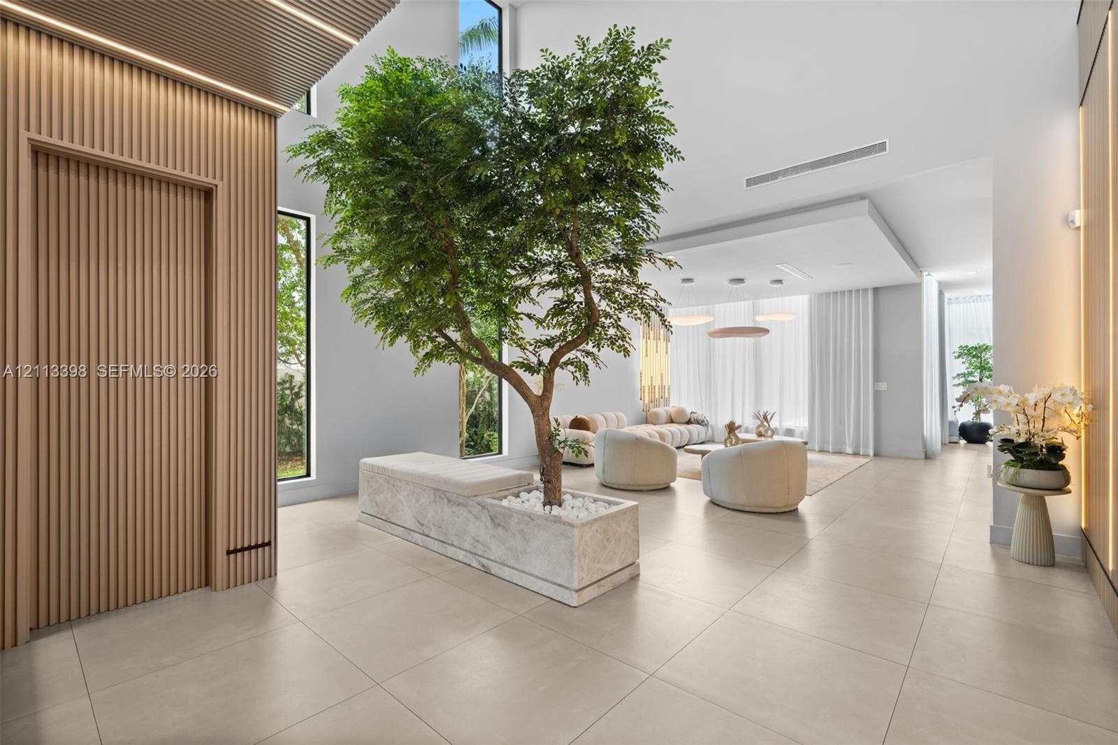 Open-concept interior featuring vertical wood-slat wall paneling, floor-to-ceiling windows, large-format tile flooring, and a built-in stone planter
