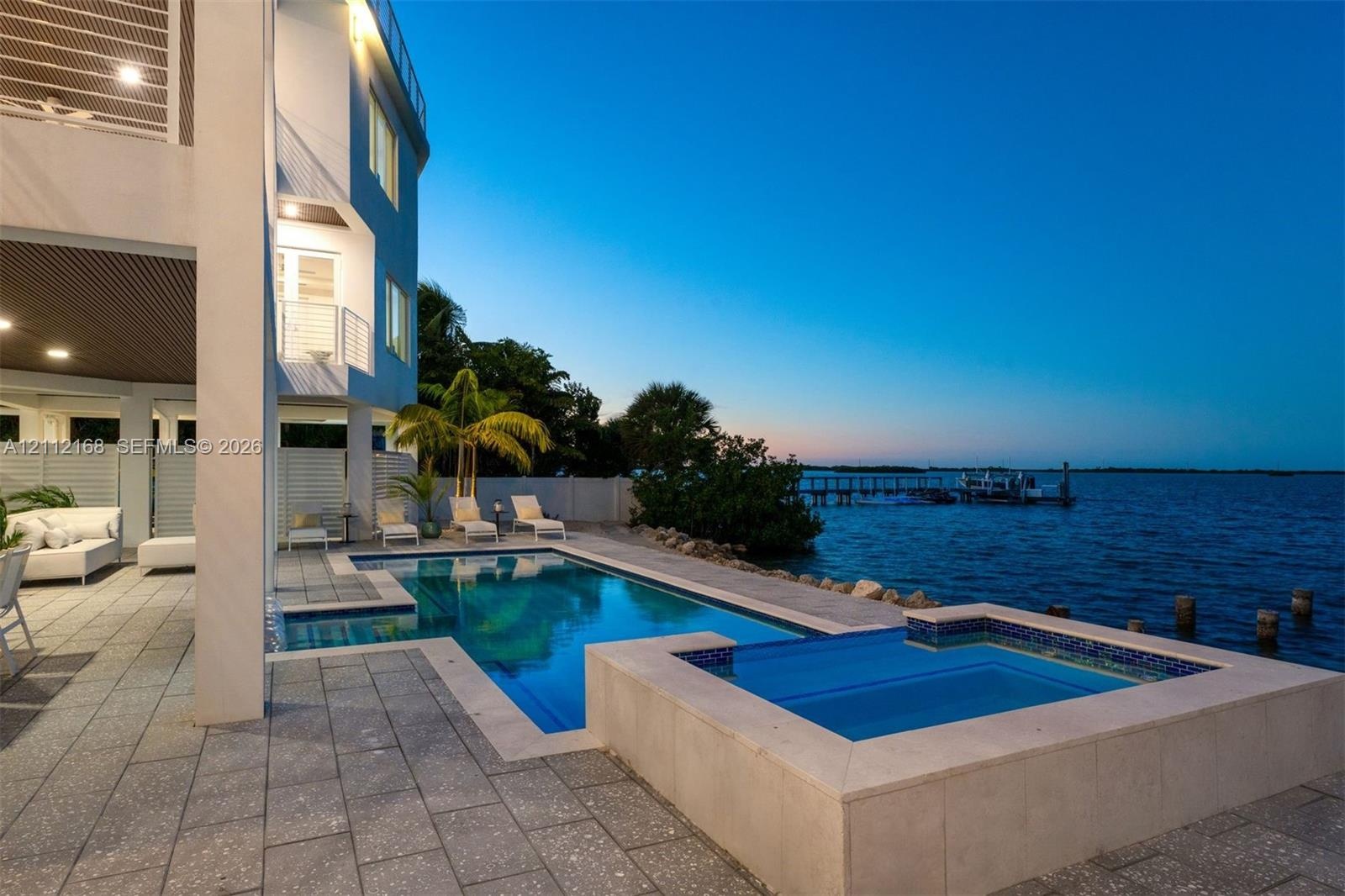 Waterfront patio featuring a concrete paver deck, built-in swimming pool, elevated spa, and multi-level balconies