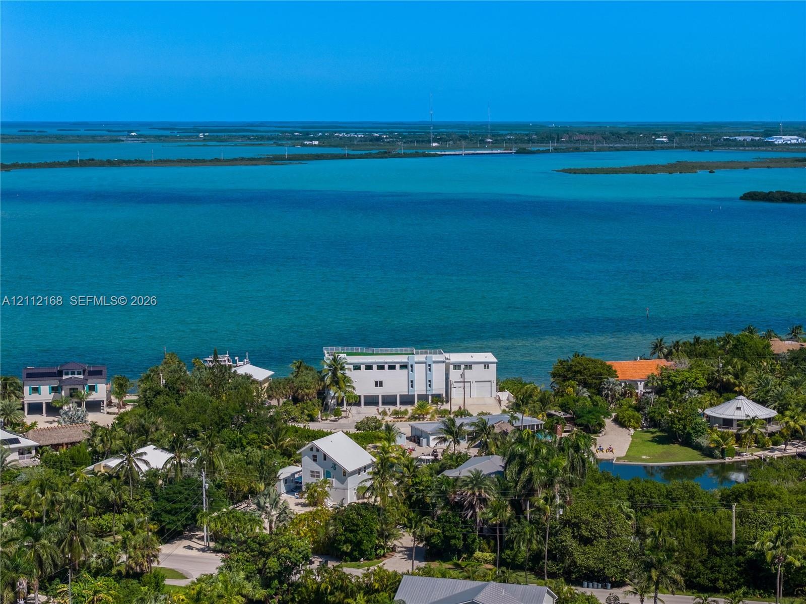 Waterfront property featuring direct coastal access, multi-level structural design, white exterior cladding, and expansive surrounding tropical vegeta